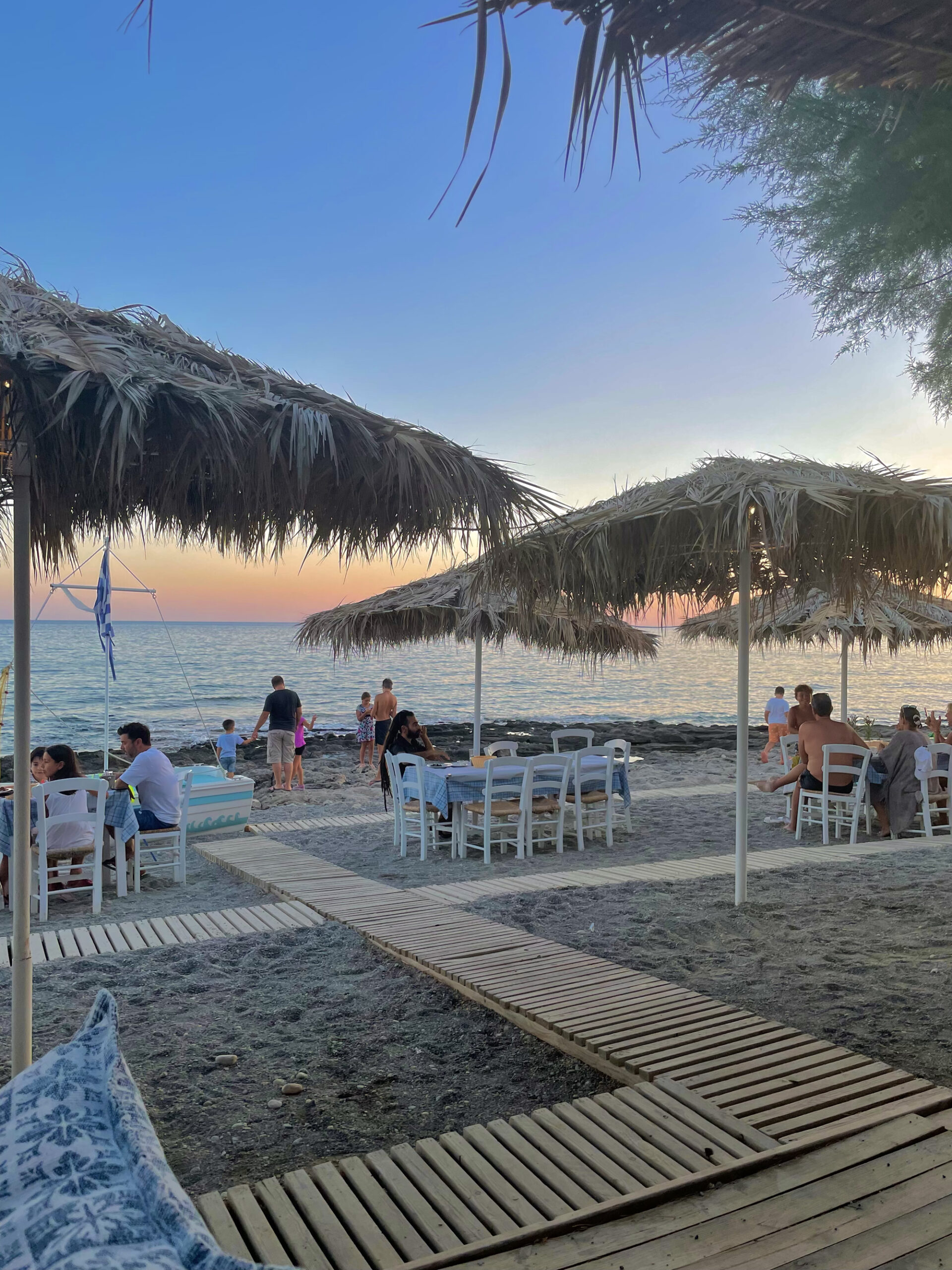 Restaurant in Griechenland am Strand mit Tischen unter Stroh-Strandschirmen